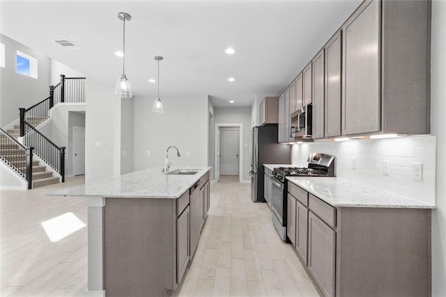 kitchen featuring sink, decorative backsplash, hanging light fixtures, a kitchen island with sink, and stainless steel appliances