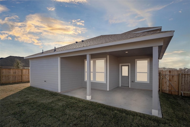 back house at dusk featuring a yard and a patio area