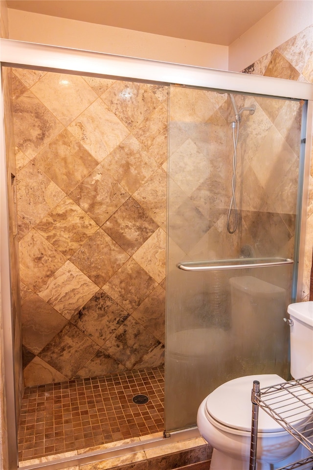 bathroom featuring a shower with door and toilet