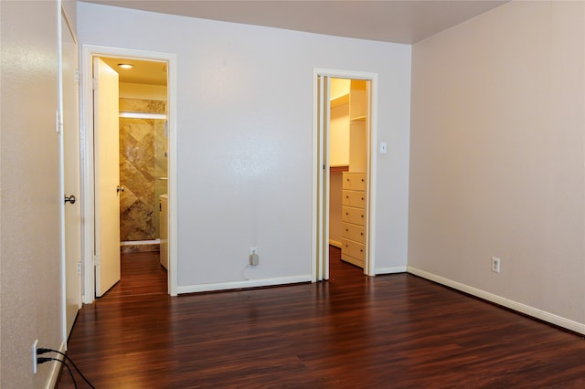 unfurnished bedroom featuring connected bathroom, a spacious closet, and dark wood-type flooring