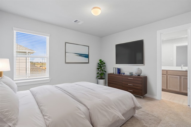 bedroom with ensuite bathroom and light colored carpet