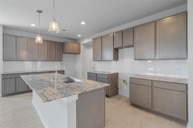 kitchen with decorative backsplash, sink, light hardwood / wood-style floors, and a kitchen island with sink