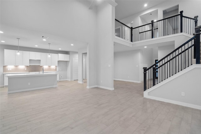 unfurnished living room featuring a towering ceiling, sink, and light hardwood / wood-style floors