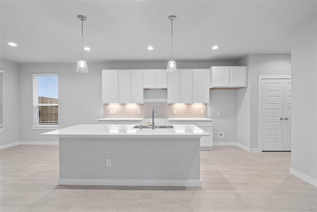 kitchen featuring pendant lighting, tasteful backsplash, sink, white cabinets, and a center island with sink