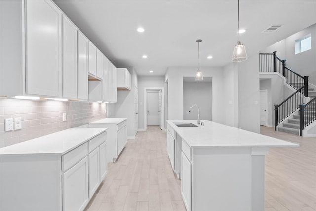 kitchen featuring a center island with sink, white cabinetry, sink, and pendant lighting