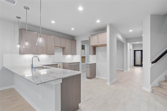 kitchen with sink, light stone counters, kitchen peninsula, pendant lighting, and decorative backsplash