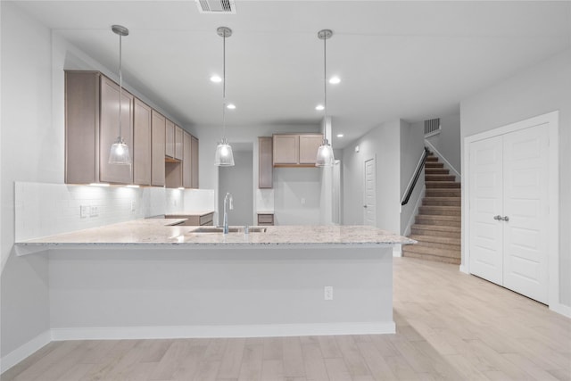 kitchen featuring pendant lighting, tasteful backsplash, sink, kitchen peninsula, and light wood-type flooring