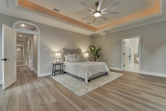 bedroom with ceiling fan, a raised ceiling, ornamental molding, and light wood-type flooring