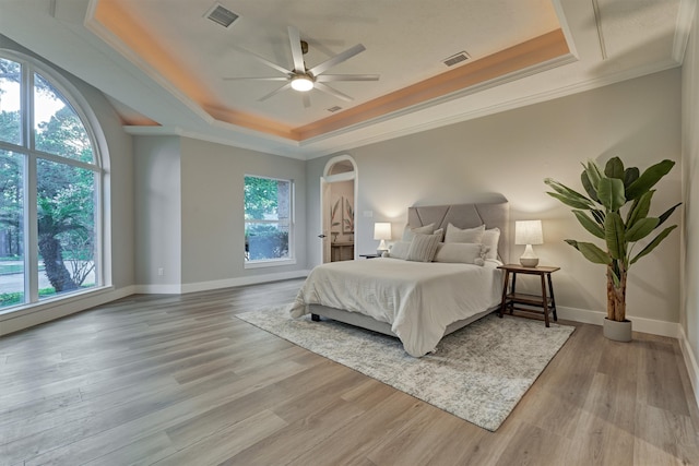 bedroom with ceiling fan, light wood-type flooring, a tray ceiling, and ornamental molding