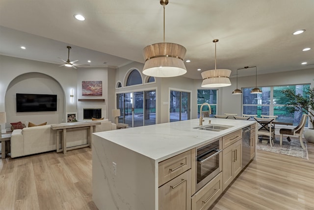 kitchen featuring appliances with stainless steel finishes, light stone counters, light hardwood / wood-style floors, sink, and a center island with sink