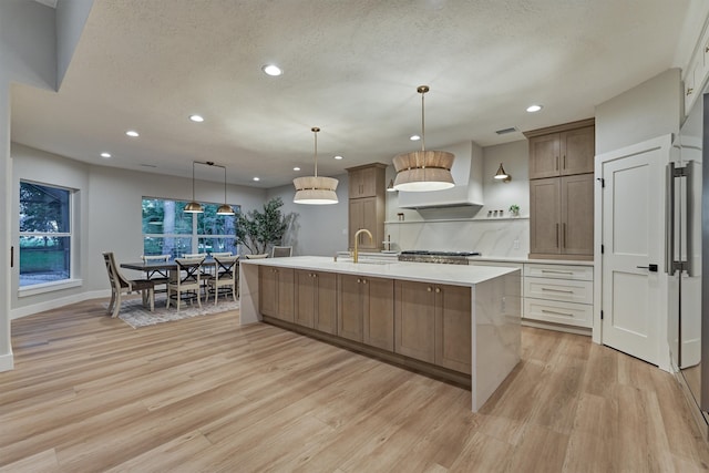 kitchen with light hardwood / wood-style flooring, an island with sink, custom exhaust hood, sink, and decorative light fixtures