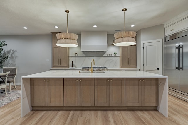 kitchen featuring custom range hood, light hardwood / wood-style floors, stainless steel built in fridge, and a spacious island