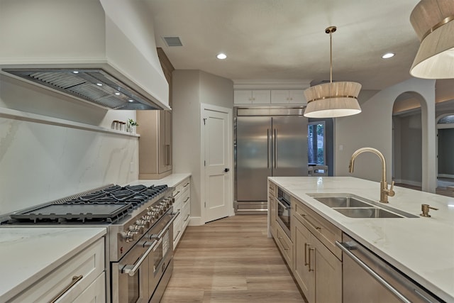 kitchen featuring custom range hood, decorative light fixtures, sink, light wood-type flooring, and high end appliances