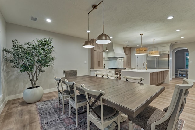 dining room with sink, a textured ceiling, and light hardwood / wood-style flooring