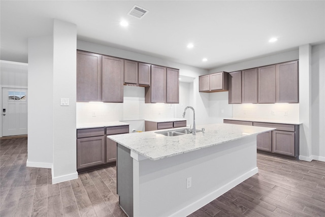 kitchen with light stone countertops, sink, hardwood / wood-style floors, and a kitchen island with sink