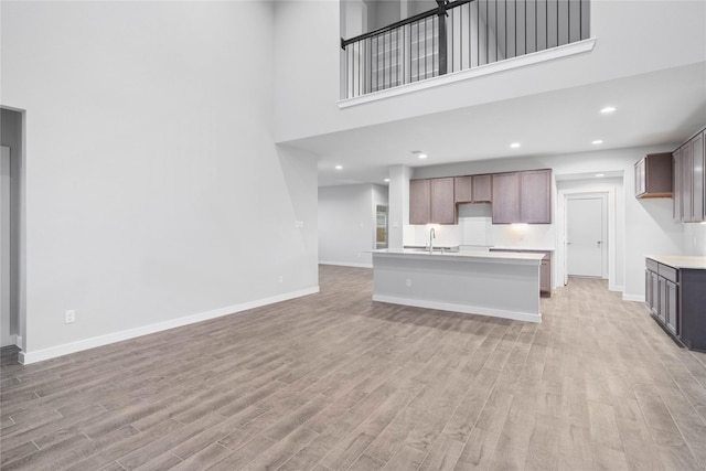 kitchen with sink, a center island with sink, light hardwood / wood-style floors, and a towering ceiling