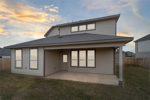 back house at dusk featuring a lawn and a patio area