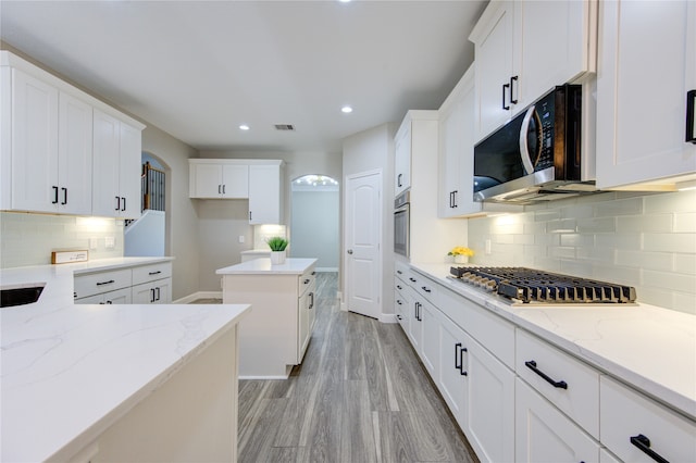 kitchen with stainless steel appliances, decorative backsplash, white cabinets, light hardwood / wood-style flooring, and light stone counters