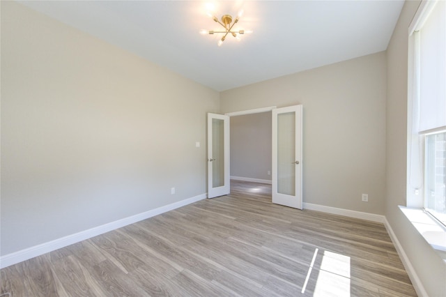 unfurnished room with an inviting chandelier, french doors, and light wood-type flooring