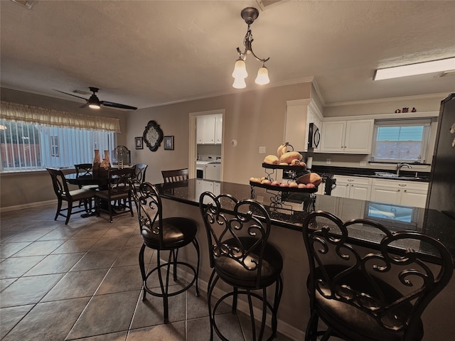 tiled dining room featuring sink, ceiling fan with notable chandelier, and ornamental molding