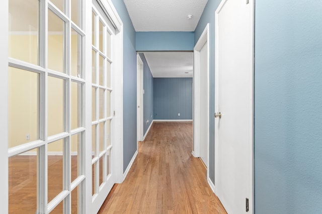 corridor with light wood-type flooring and a textured ceiling