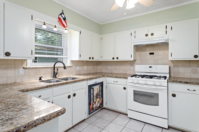 kitchen featuring white gas stove, decorative backsplash, ceiling fan, white cabinets, and sink