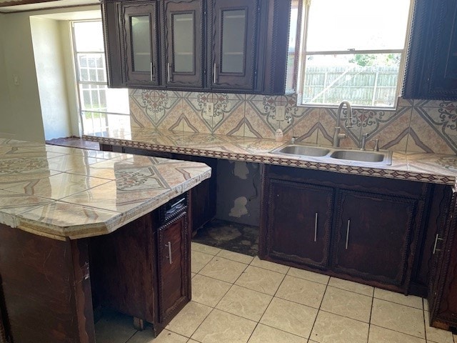 kitchen featuring sink, decorative backsplash, light tile patterned floors, and dark brown cabinets