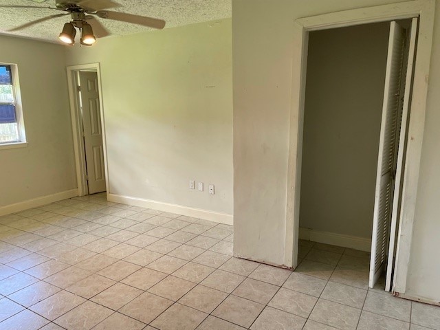 unfurnished bedroom featuring ceiling fan, a closet, a textured ceiling, and light tile patterned floors