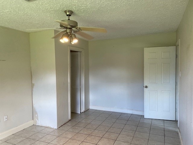 unfurnished bedroom featuring a textured ceiling, a closet, ceiling fan, and light tile patterned flooring