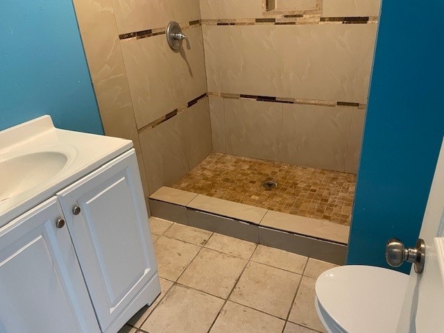 bathroom with toilet, a tile shower, vanity, and tile patterned floors