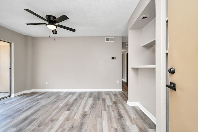 empty room with a textured ceiling, ceiling fan, built in features, and light hardwood / wood-style floors