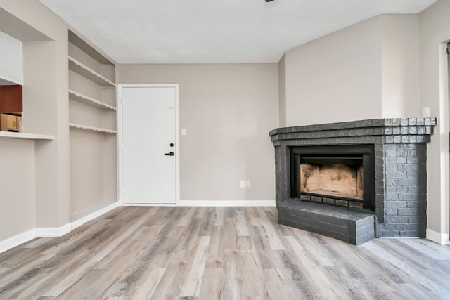 unfurnished living room with a fireplace, a textured ceiling, wood-type flooring, and built in shelves