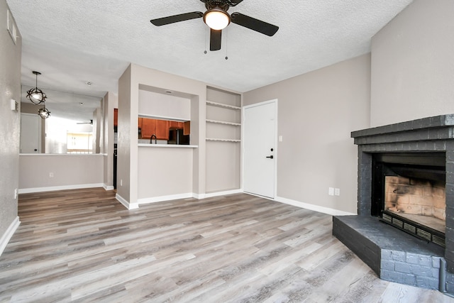 unfurnished living room featuring a textured ceiling, wood-type flooring, and a brick fireplace