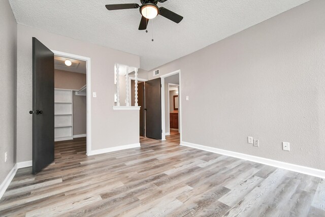 unfurnished bedroom with hardwood / wood-style floors, a walk in closet, a closet, ceiling fan, and a textured ceiling