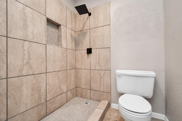 bathroom with toilet, a tile shower, and tile patterned floors