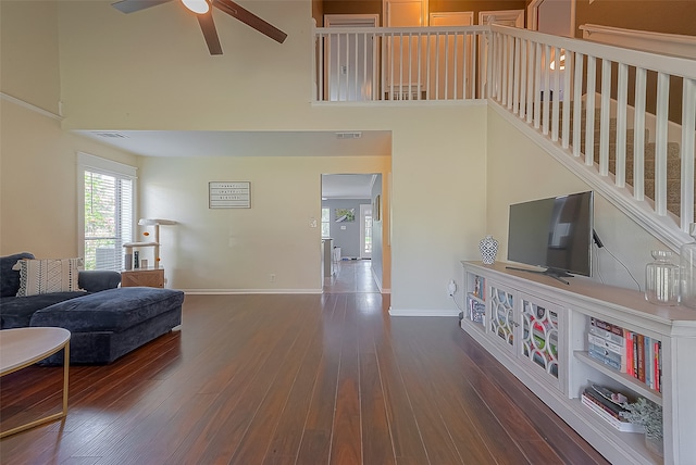 living room with ceiling fan, dark wood-type flooring, and a towering ceiling