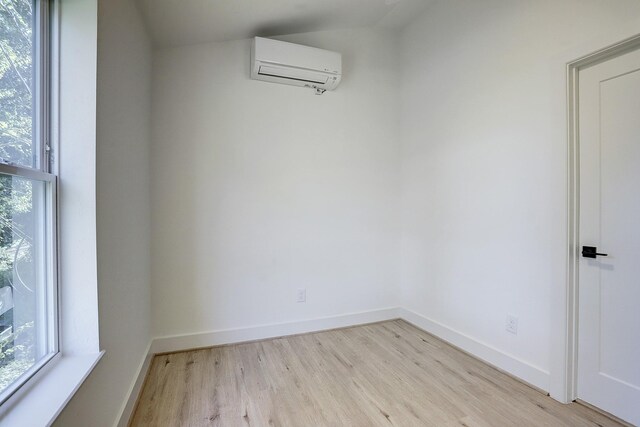 unfurnished room featuring plenty of natural light, light wood-type flooring, and a wall mounted air conditioner