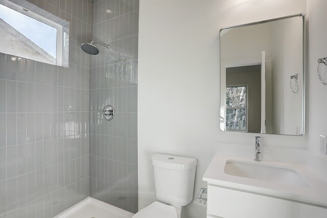 bathroom featuring toilet, tiled shower, and vanity