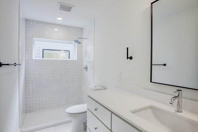 bathroom featuring toilet, a tile shower, vanity, and tile patterned floors