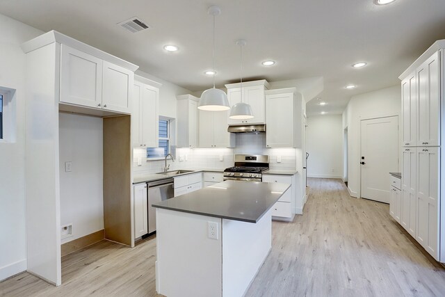 kitchen with light wood-type flooring, hanging light fixtures, appliances with stainless steel finishes, white cabinetry, and a center island