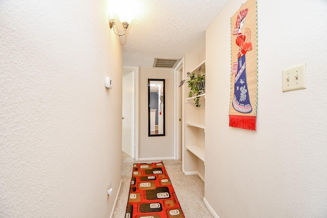 hallway with carpet flooring, a textured ceiling, visible vents, and baseboards