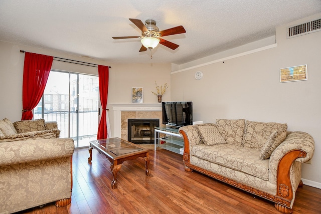 living area featuring a tiled fireplace, ceiling fan, hardwood / wood-style flooring, and visible vents