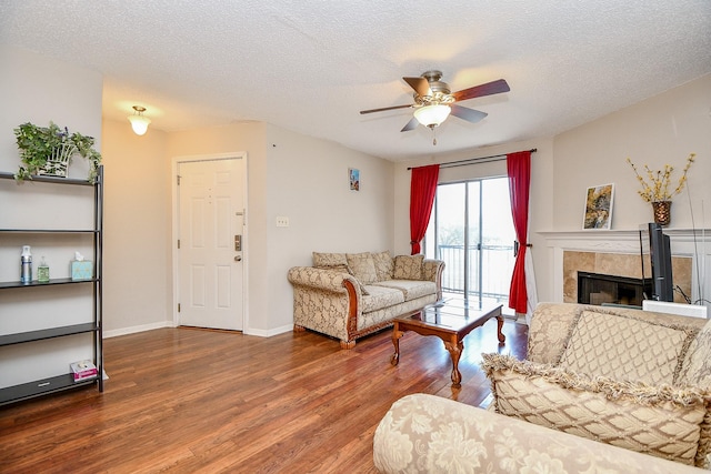 living room with a ceiling fan, a textured ceiling, wood finished floors, and a fireplace