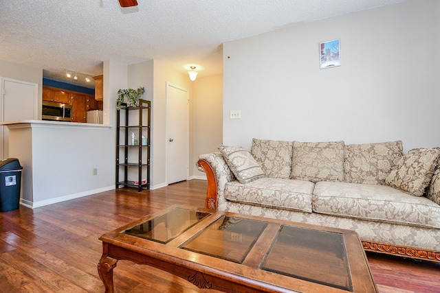 living room featuring ceiling fan, a textured ceiling, rail lighting, wood finished floors, and baseboards