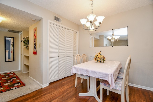 dining space with a textured ceiling, visible vents, wood finished floors, baseboards, and a notable chandelier