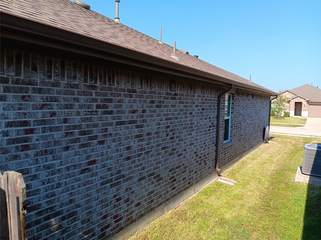 view of side of home with a shingled roof, brick siding, a lawn, and central air condition unit