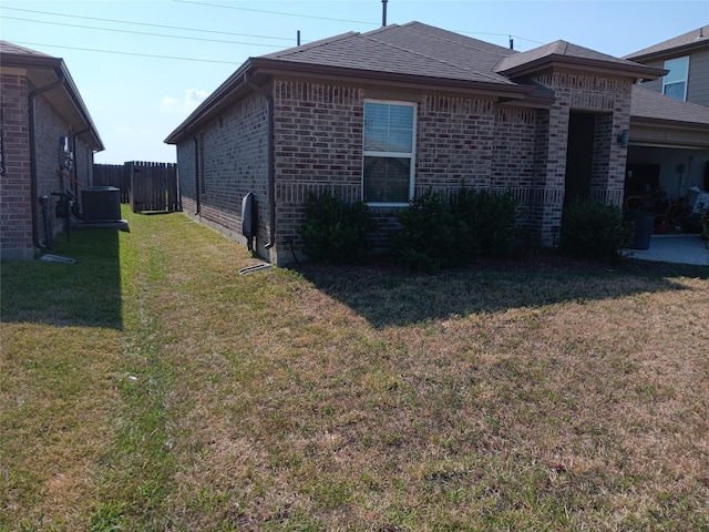 view of property exterior with a shingled roof, brick siding, a yard, and fence