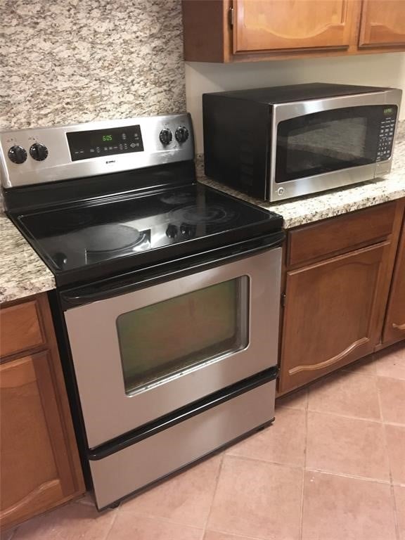 kitchen featuring light tile patterned floors, stainless steel appliances, and light stone counters