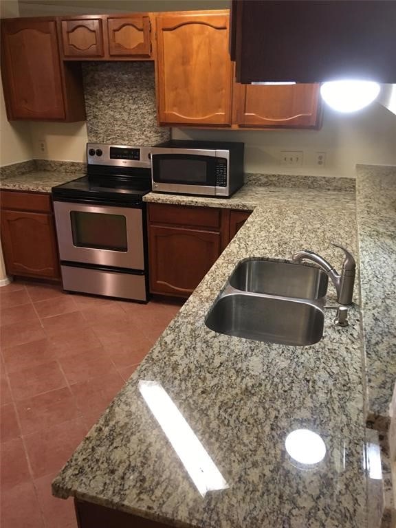 kitchen with light stone countertops, sink, stainless steel appliances, and tile patterned flooring