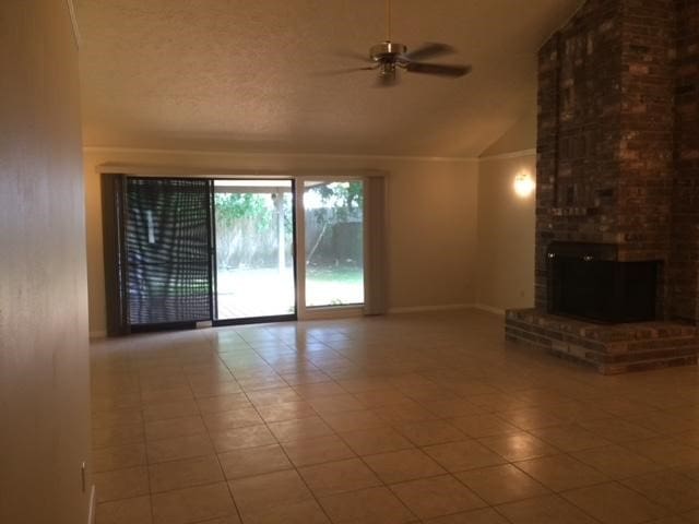 unfurnished living room featuring brick wall, tile patterned floors, a fireplace, lofted ceiling, and ceiling fan